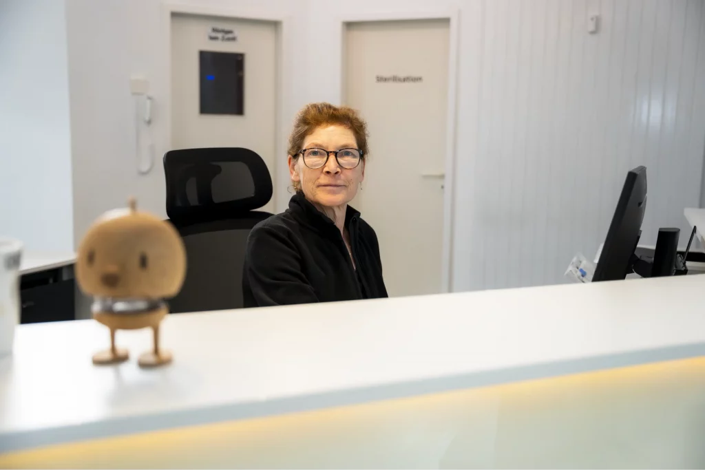 Empfangsbereich der Zahnarztpraxis Zahnfreunde Euskirchen mit freundlicher Mitarbeiterin am Empfangstresen in moderner, heller Praxisumgebung.
