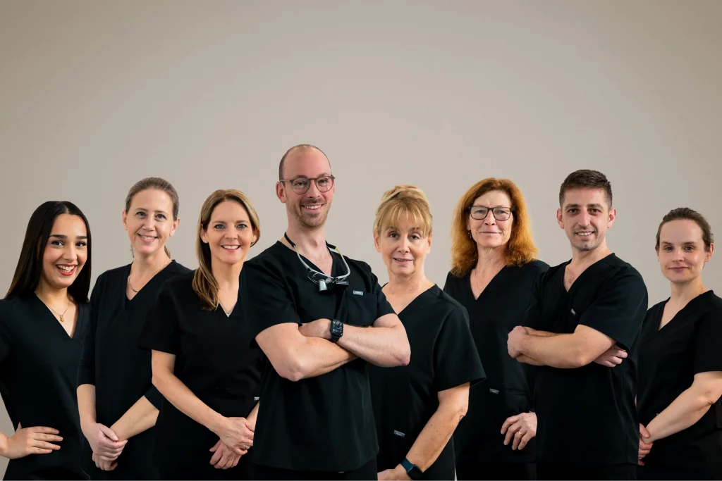 Gruppenfoto des Teams der Zahnarztpraxis Zahnfreunde Euskirchen mit Zahnärzten und Mitarbeitenden in schwarzer Arbeitskleidung vor neutralem Hintergrund.